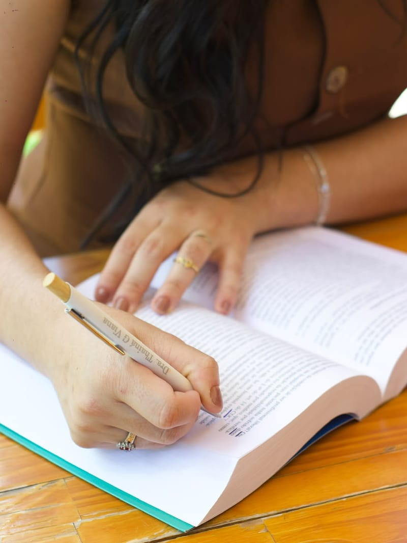 Profissional escrevendo em um livro aberto, detalhe das mãos e da caneta personalizada